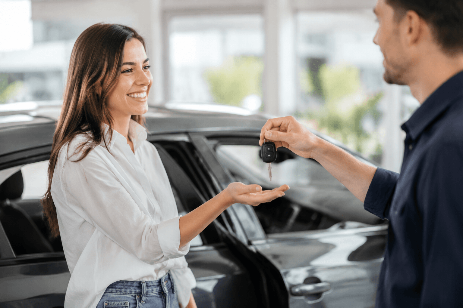 A salesperson handing car keys to a smiling new driver beside a car